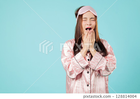 Eye mask cover for woman sleep, young asian portrait with routine for sleep, she plans her beauty nap to rest and relax in her pajamas for a good night rest, headshot isolated studio blue background 128814004