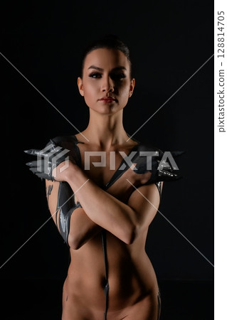 Confident woman poses creatively with striking body art in dark setting Confident woman poses creatively with striking body art in dark setting 128814705