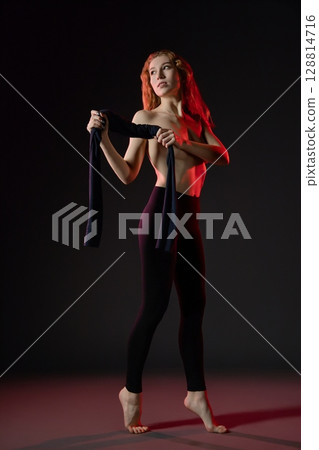Woman dancing gracefully in a dark studio with dramatic lighting Woman dancing gracefully in a dark studio with dramatic lighting 128814716