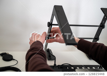 person adjusting ergonomic metal laptop stand on white desk in home office  128815448