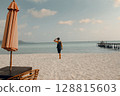 A lone person walking on the sandy beach with an umbrella and wicker chair on the foreground and the ocean in the background. Koh Rong Sanloem, Sihanoukville, Cambodia 128815603