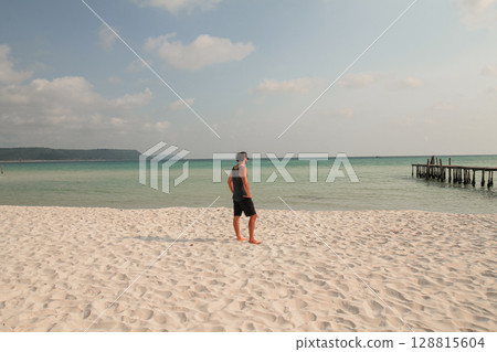 A man stands on a sandy beach looking out at the calm ocean in Koh Rong Sanloem, Sihanoukville, Cambodia 128815604