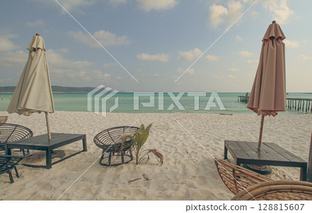 A serene beach setting with umbrellas, lounge chairs, and calm sea under a cloudy sky in Koh Rong Sanloem, Sihanoukville, Cambodia 128815607