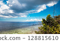 A wide ocean view framed by greenery in the foreground, dynamic clouds, and a bright blue summer sky. Siquijor island, Philippines 128815610