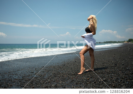 Woman stands on black sand beach enjoying the warm sun Woman stands on black sand beach enjoying the warm sun 128816204