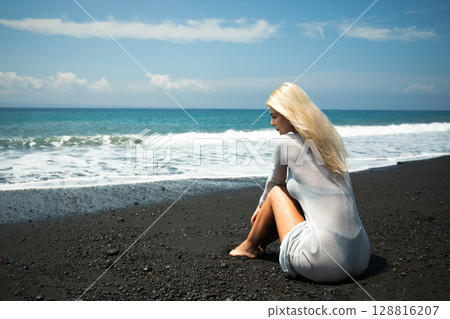 Woman on sandy shore gazing at waves and skyline Woman on sandy shore gazing at waves and skyline 128816207