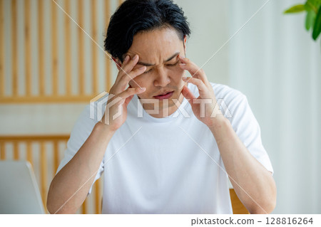 Man holding his head while using a laptop Man holding his head while using a laptop 128816264