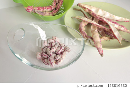 Pink kidney bean pods and beans in glass bowl on kitchen table. Healthy food and vegetables. Organic seasonal farm products. Pink kidney bean pods and beans in glass bowl on kitchen table. Healthy food and vegetables. Organic seasonal farm products. 128816880
