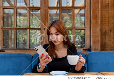 Young woman drinking coffee and reading phone at outdoor caf 128817799