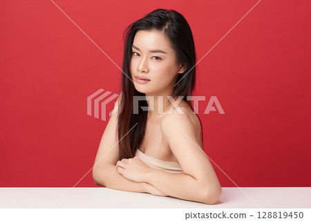 A beautiful young Asian woman with clean, fresh skin against a red background. Skincare, facial treatment, cosmetology, beauty, and spa. An elegant portrait of an Asian woman. 128819450