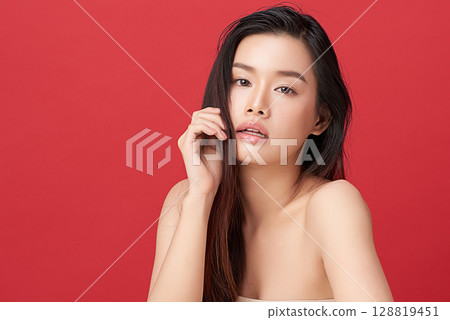 A beautiful young Asian woman with clean, fresh skin against a red background. Skincare, facial treatment, cosmetology, beauty, and spa. An elegant portrait of an Asian woman. 128819451