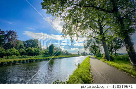 A Serene and Beautiful Canal View Surrounded by Lush Greenery Beneath a Bright Blue Sky 128819671