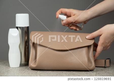 Care of leather products. Applying a special spray of the product to the surface of a leather handbag. 128819691