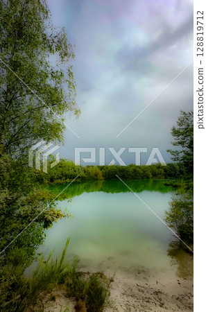 A Serene and Picturesque Lakeside View Surrounded by Lush Greenery and a Dramatic Sky A Serene and Picturesque Lakeside View Surrounded by Lush Greenery and a Dramatic Sky 128819712