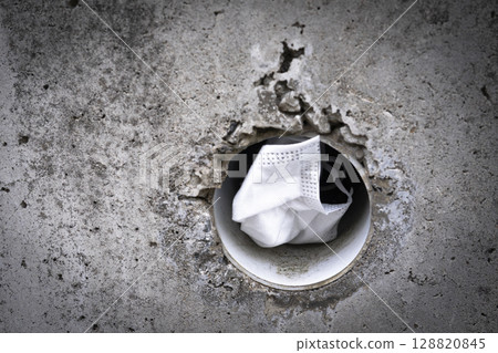 一張被丟棄在混凝土牆排水孔中的口罩的照片 128820845