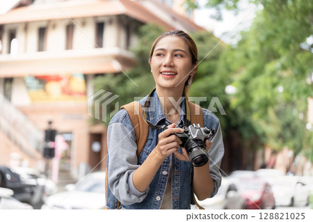 Happy young woman photographer exploring city with camera Happy young woman photographer exploring city with camera 128821025