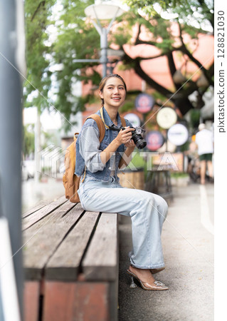 Content woman photographer sitting on bench in urban setting Content woman photographer sitting on bench in urban setting 128821030