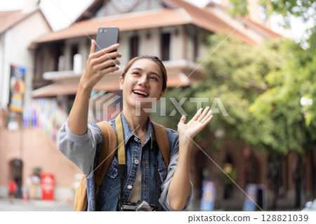 Cheerful young woman taking selfie with smartphone outdoors 128821039