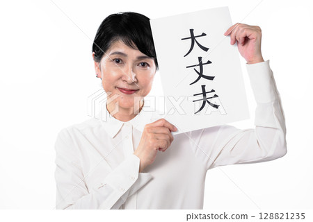 一位年長的女性微笑著，手裡拿著一張寫著「好的」的紙 128821235