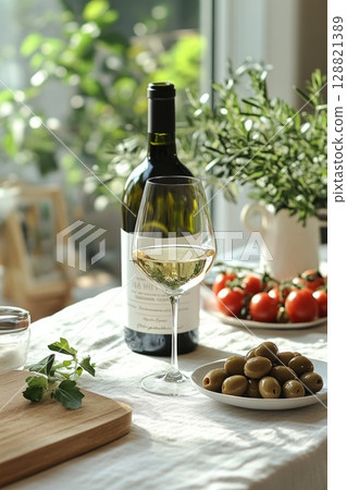 White wine, olives, and herbs on a sunlit table next to a large window, great for wellness, healthy eating, and fresh summer food concepts. 128821389