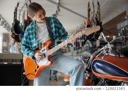 A woman plays guitar while sitting on a motorcycle 128821563