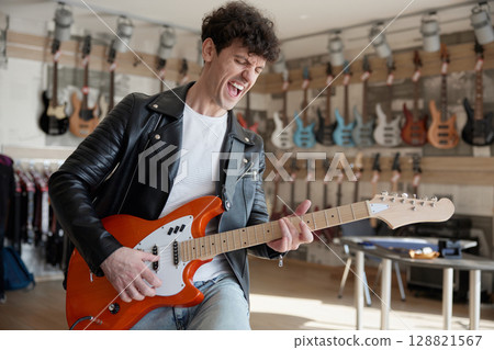 A man in a leather jacket is playing guitar in a store 128821567
