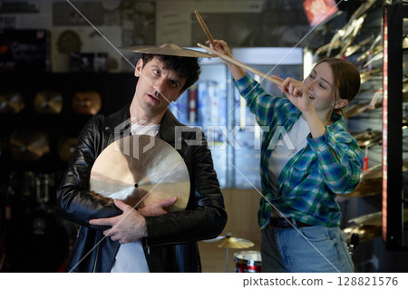 A man holds a cymbal while a woman holds drumsticks 128821576