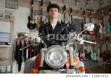 A confident biker poses in a bustling music store surrounded by numerous guitars A confident biker poses in a bustling music store surrounded by numerous guitars 128821615