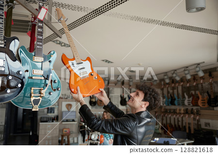 Musician intently exploring various electric guitars in a vibrant music store 128821618