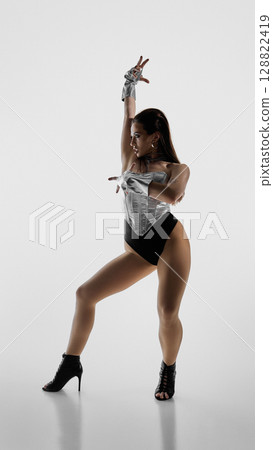 Dancer strikes jazz funk pose wearing metallic outfit and high heels 128822419