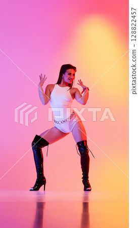 Dancer striking a pose in vibrant lighting and stylish high-heeled boots Dancer striking a pose in vibrant lighting and stylish high-heeled boots 128822457