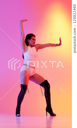 Performer in white attire and high heels poses against vibrant gradient backdrop Performer in white attire and high heels poses against vibrant gradient backdrop 128822460