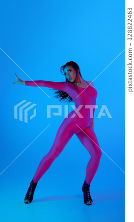 Dancer in vibrant pink bodysuit strikes pose with blue background 128822463