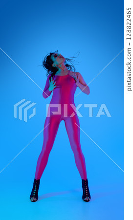 Woman in pink catsuit dancing with high heels against blue background 128822465