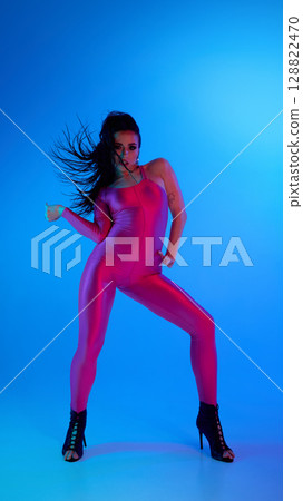 Dancer in pink bodysuit and high heels striking a pose under blue lighting 128822470