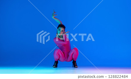 Woman dancing jazz funk in pink outfit and high heels against blue background 128822484