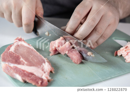 Person's hands expertly dicing raw fresh pork meat into small, uniform pieces on a green cutting board, highlighting food preparation and healthy cooking Person's hands expertly dicing raw fresh pork meat into small, uniform pieces on a green cutting board, highlighting food preparation and healthy cooking 128822870