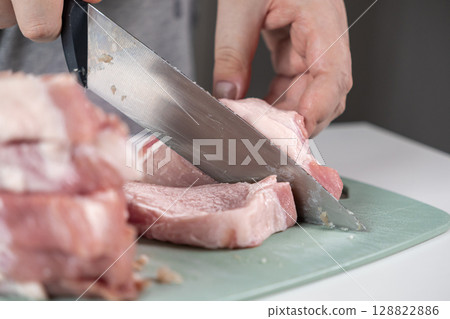 A person's hand precisely slicing fresh raw pork loin on a green cutting board, essential for home cooking and healthy meal preparation 128822886
