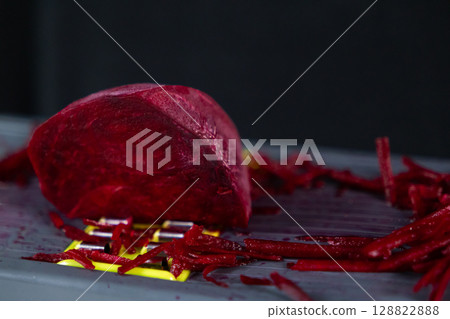 Fresh vibrant red beetroot being grated on a modern yellow and gray kitchen grater, highlighting healthy vegetable preparation for natural cooking and culinary dishes Fresh vibrant red beetroot being grated on a modern yellow and gray kitchen grater, highlighting healthy vegetable preparation for natural cooking and culinary dishes 128822888