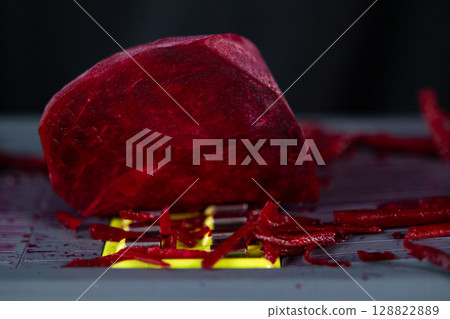 Vibrant red peeled beet being freshly grated on a mandoline, creating colorful shredded pieces, symbolizing healthy eating and nutritious natural ingredients Vibrant red peeled beet being freshly grated on a mandoline, creating colorful shredded pieces, symbolizing healthy eating and nutritious natural ingredients 128822889