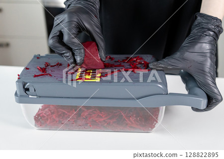 Gloved hands skillfully using a kitchen mandoline grater to shred vibrant beetroot, perfect for healthy recipes and efficient meal preparation Gloved hands skillfully using a kitchen mandoline grater to shred vibrant beetroot, perfect for healthy recipes and efficient meal preparation 128822895