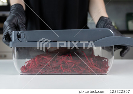 Chef's gloved hands expertly operating a modern kitchen vegetable grater, efficiently preparing fresh, vibrant red shredded beetroots for healthy and delicious meals Chef's gloved hands expertly operating a modern kitchen vegetable grater, efficiently preparing fresh, vibrant red shredded beetroots for healthy and delicious meals 128822897