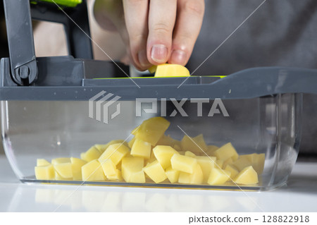 A hand operates a modern vegetable dicer, efficiently preparing fresh diced potatoes for cooking, demonstrating smart kitchen convenience and healthy meal prep A hand operates a modern vegetable dicer, efficiently preparing fresh diced potatoes for cooking, demonstrating smart kitchen convenience and healthy meal prep 128822918