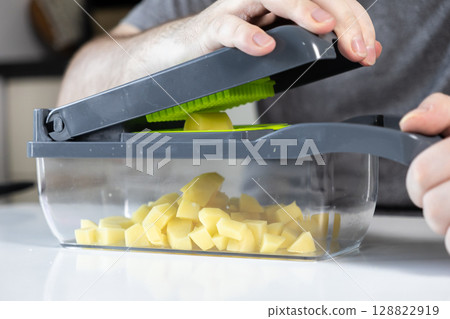 Person using a practical kitchen vegetable chopper to quickly cube fresh raw potatoes, showcasing efficient food preparation and healthy home cooking 128822919