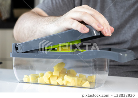 Man operating a kitchen vegetable chopper, efficiently dicing potatoes for home cooking, highlighting convenience and healthy meal preparation Man operating a kitchen vegetable chopper, efficiently dicing potatoes for home cooking, highlighting convenience and healthy meal preparation 128822920