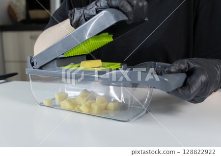 Person in protective gloves efficiently using a manual vegetable chopper to dice raw potatoes, promoting quick and safe food preparation in a modern kitchen Person in protective gloves efficiently using a manual vegetable chopper to dice raw potatoes, promoting quick and safe food preparation in a modern kitchen 128822922