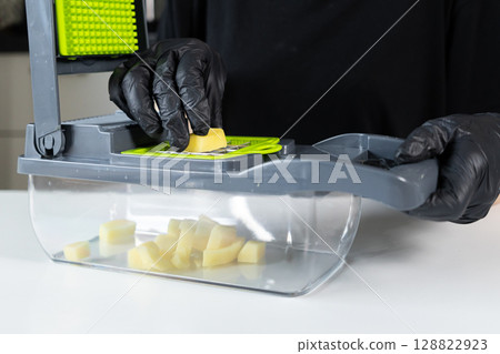 A person wearing black gloves actively uses a multi-functional kitchen vegetable chopper, dicing fresh potatoes, illustrating efficient home food preparation for nutritious meals easily A person wearing black gloves actively uses a multi-functional kitchen vegetable chopper, dicing fresh potatoes, illustrating efficient home food preparation for nutritious meals easily 128822923