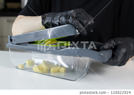 Person in black gloves uses a manual vegetable chopper, expertly dicing potatoes into uniform pieces for convenient home meal preparation and efficient healthy cooking Person in black gloves uses a manual vegetable chopper, expertly dicing potatoes into uniform pieces for convenient home meal preparation and efficient healthy cooking 128822924