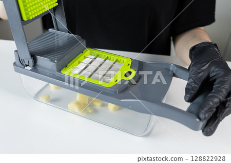 Gloved person uses a modern grey and green kitchen vegetable chopper, efficiently dicing raw potatoes for quick food preparation and convenient healthy cooking Gloved person uses a modern grey and green kitchen vegetable chopper, efficiently dicing raw potatoes for quick food preparation and convenient healthy cooking 128822928