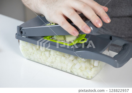 Human hand operating a modern kitchen vegetable chopper, efficiently dicing fresh white onions, simplifying quick healthy meal preparation Human hand operating a modern kitchen vegetable chopper, efficiently dicing fresh white onions, simplifying quick healthy meal preparation 128822937